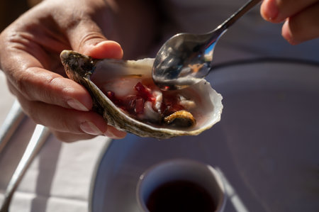Young woman in white dress eats fresh live creuze oysters with marinated onion, seafood in French restaurantの写真素材