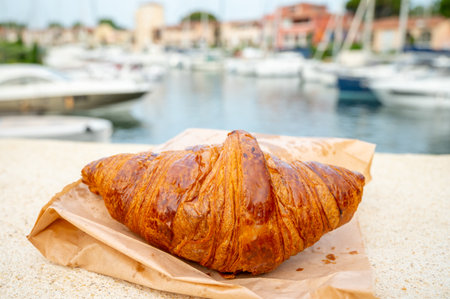 Fresh baked french croissant and boats of Port Grimaud on background, lifestyle in south of Franceの写真素材