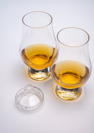 Tulip-shaped tasting glass with dram of Scotch single malt or blended whiskey on white background,...