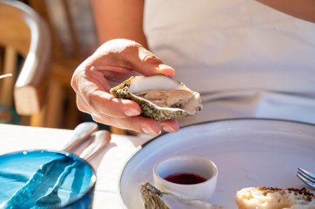 Young woman in white dress eats fresh live creuze oysters with marinated onion, seafood in French restaurantの写真素材