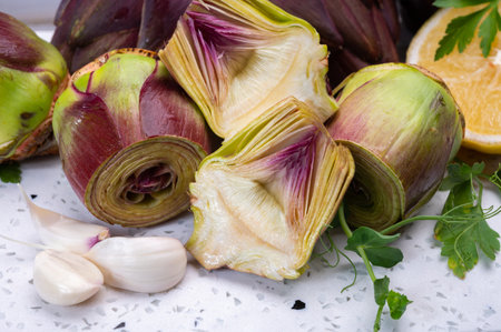 Raw fresh purple romanesco artichoke vegetable heads and pilled hearts ready to cook, young garlic and parsleyの写真素材