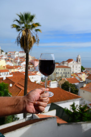 Hand with glass of dry red Portuguese wine in outdoor cafe at view point on colorful old part of Lisbon city, Portugalの写真素材