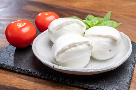 White balls of Italian soft cheese Mozzarella di Bufala Campana served with fresh green basil leaves and red tomatoの写真素材