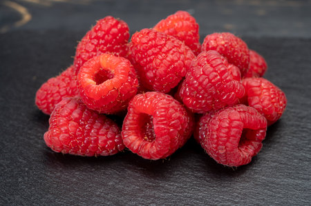 Fresh organic fruit - ripe red sweet raspberry on dark background close up