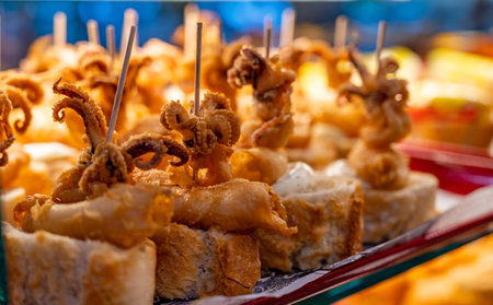 Typical snack of Basque Country, pinchos or pinxtos skewers with small pieces of bread, sea food, baby octopus, cheese, jamon served in bar in San-Sebastian or Bilbao, Spain, close upの写真素材