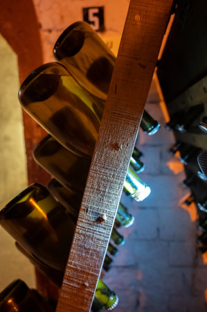 Walking in deep long undergrounds caves with dusty bottles on racks, making champagne sparkling wine...