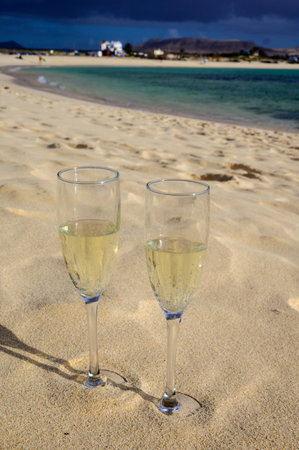 Two glasses of white champagne or cava sparkling wine served on white sandy tropical beach and blue ocean, romantic vacation, winter sun on Fuerteventura, Il Cotillo, Canary, Spainの写真素材