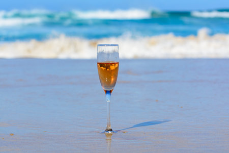 One glass of rose champagne or cava sparkling wine served on white sandy tropical beach and blue ocean water, romantic vacation, winter sun on Fuerteventura, Canary, Spainの写真素材