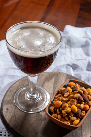 Glass of Belgian abbey red brown beer and glass bowl with party nuts, close upの写真素材