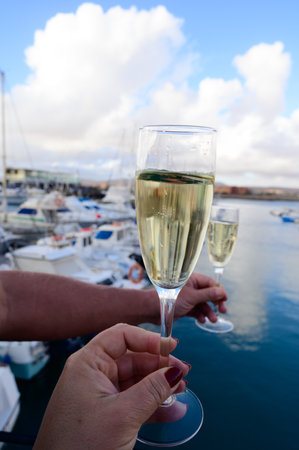 Everyday party, hands with glasses of cava or champagne sparkling wine in yacht harbor of Caleta de Fuste, Fuerteventura, Canary islands vacation, Spainの写真素材