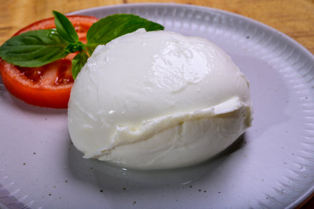 White ball of Italian soft cheese Mozzarella di Bufala Campana served with fresh green basil and red...