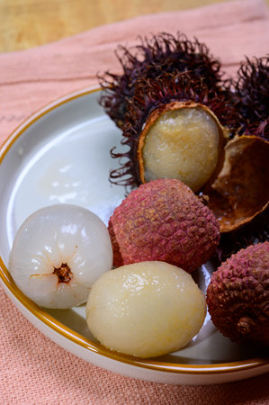 Tasty tropical exotic fruits, sweet ripe fresh peeled and unpeeled ychee and hairy rambutan southeast Asian fruits, close upの写真素材