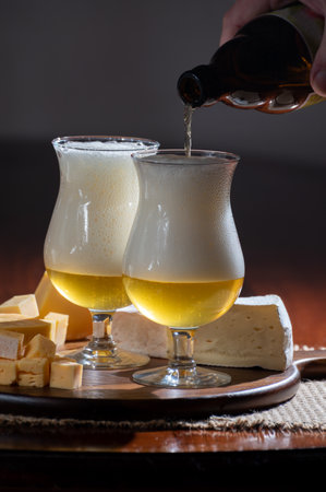 Pouring of Belgian light blonde beer made in abbey and wooden board with variety of belgian cheeses, food and beer pairingの写真素材