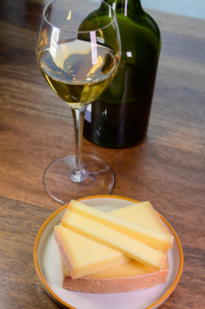 Wine and cheese pairing, local Comte cheese produced in the Franche-Comte region and glass and clavelin bottle special and characteristic yellow wine vin jaune from Jura region, Franceの写真素材