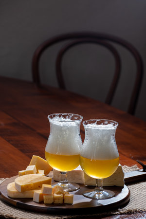 Glasses of Belgian light blonde beer made in abbey and wooden board with variety of belgian cheeses, food and beer pairingの写真素材