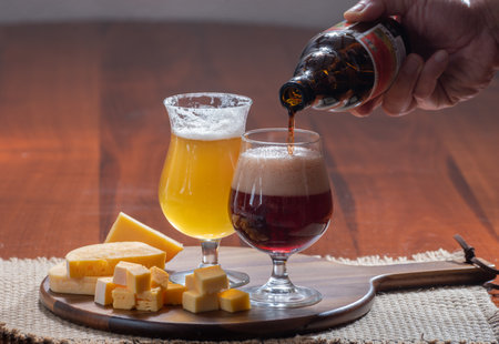 Glasses of Belgian yellow blond and dark brown beer made in abbey and wooden board with variety of belgian cheeses, food and beer pairing in Belgiumの写真素材