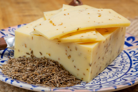 Cheese of Netherlands, piece of cow milk Dutch gouda cheese with dried aromatic cumin seeds close up