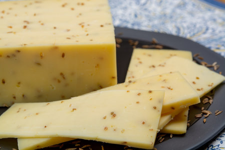Cheese of Netherlands, piece of cow milk Dutch gouda cheese with dried aromatic cumin seeds close up