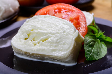 Sliced white ball of Italian soft cheese Mozzarella di Bufala Campana served with fresh green basil and red tomato, close upの写真素材