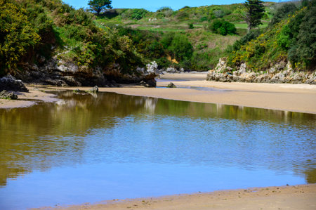 View on Playa de Poo during low tide near Llanes, Green coast of Asturias, North Spain with white sandy beaches, cliffs, hidden caves, green fields and mountains.の写真素材
