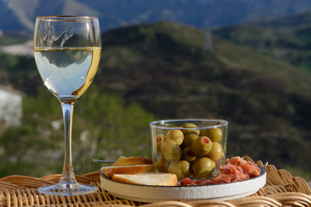 Drinking of dry white wine and spanish tapas olives in bowl with mountains peaks on background in sunny dayの写真素材