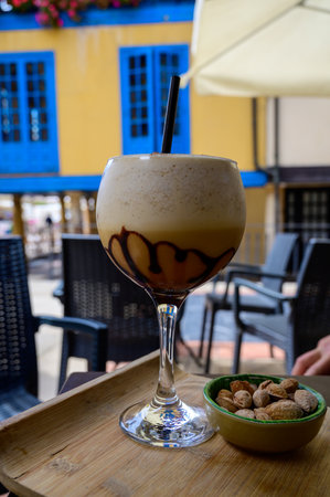 Glaass of iced coffee with whipped cream, chocolate and ice cubes served in outdoor cafe in Oviedo,...