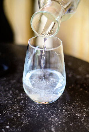 Waiter pouring mineral water from the glass bottle into a glass, food concept close up