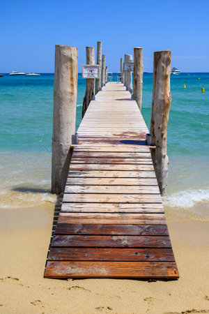 Wooden pier and crystal clear blue water of legendary Pampelonne beach near Saint-Tropez, summer vacation on French Riviera, France, text translation: it's dangerous not to dive off pier.の写真素材