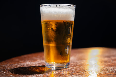 Pint glass of cold fresh british ale and lager beer served in old vintage English pub, dark...