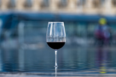 Tasting of Bordeaux blended red wine with wine city Bordeaux on background, left bank of Gironde Estuary, France. Glass of red French wine served outdoor.の写真素材