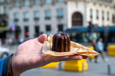 Canele, French pastry flavored with rum and vanilla, soft and tender custard center and dark, caramelized crust specialty of Bordeaux region, France and streets of Bordeaux on backgroundの写真素材