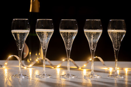 New year party, pouring of brut champagne bubbles cava or prosecco wine in tulip glasses with garland lights on dark backgroundの写真素材