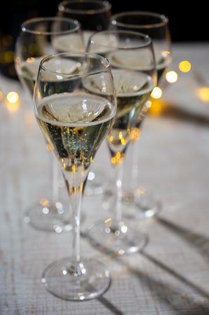 New year party, small bubbles of brut champagne cava or prosecco wine in tulip glasses with garland lights on dark backgroundの写真素材