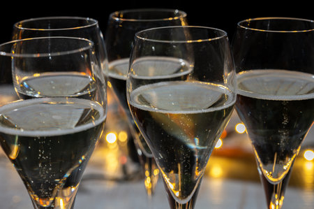 New year party, small bubbles of brut champagne cava or prosecco wine in tulip glasses with garland lights on dark backgroundの写真素材