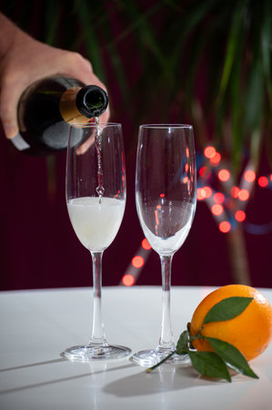 Pouring of brut champagne, cava or prosecco dry wine in glasses with garland lights on dark background, new year or birthday partyの写真素材