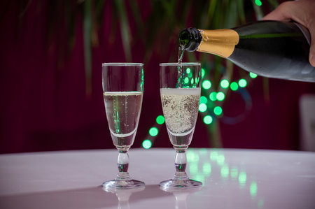 Pouring of brut champagne, cava or prosecco dry wine in glasses with garland lights on dark background, new year or birthday partyの写真素材