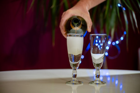 Pouring of brut champagne, cava or prosecco dry wine in glasses with garland lights on dark background, new year or birthday partyの写真素材