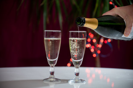 Pouring of brut champagne, cava or prosecco dry wine in glasses with garland lights on dark background, new year or birthday partyの写真素材