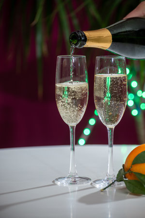 Pouring of brut champagne, cava or prosecco dry wine in glasses with garland lights on dark background, new year or birthday partyの写真素材