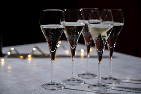 New year party, small bubbles of brut champagne cava or prosecco wine in tulip glasses with garland lights on dark backgroundの写真素材