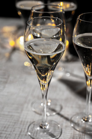 New year party, small bubbles of brut champagne cava or prosecco wine in tulip glasses with garland lights on dark backgroundの写真素材