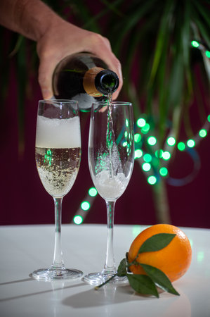 Pouring of brut champagne, cava or prosecco dry wine in glasses with garland lights on dark background, new year or birthday partyの写真素材