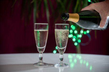 Pouring of brut champagne, cava or prosecco dry wine in glasses with garland lights on dark background, new year or birthday partyの写真素材