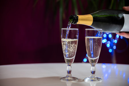 Pouring of brut champagne, cava or prosecco dry wine in glasses with garland lights on dark background, new year or birthday partyの写真素材