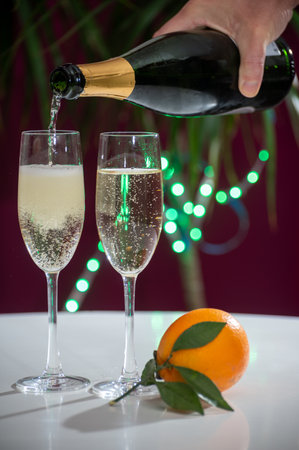 Pouring of brut champagne, cava or prosecco dry wine in glasses with garland lights on dark background, new year or birthday partyの写真素材