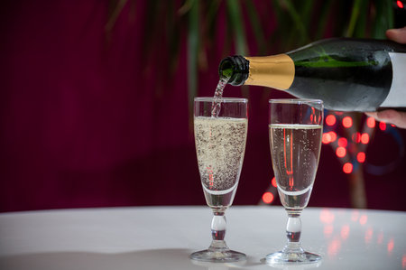 Pouring of brut champagne, cava or prosecco dry wine in glasses with garland lights on dark background, new year or birthday partyの写真素材