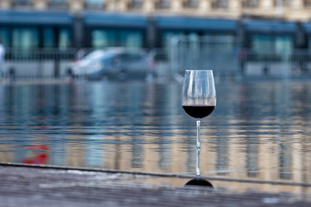 Tasting of Bordeaux blended red wine with wine city Bordeaux on background, left bank of Gironde Estuary, France. Glass of red French wine served outdoor.の写真素材