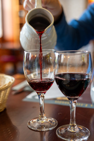 Pouring yound red beaujolais wine in glasses during celebration of end of harvest and first sale release on third Thursday of November from white ceramic pitcher in Limouges, Franceの写真素材