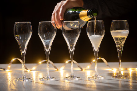 New year party, pouring of brut champagne bubbles cava or prosecco wine in tulip glasses with garland lights on dark backgroundの写真素材