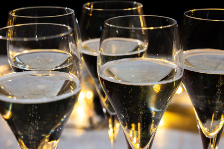 New year party, small bubbles of brut champagne cava or prosecco wine in tulip glasses with garland lights on dark backgroundの写真素材